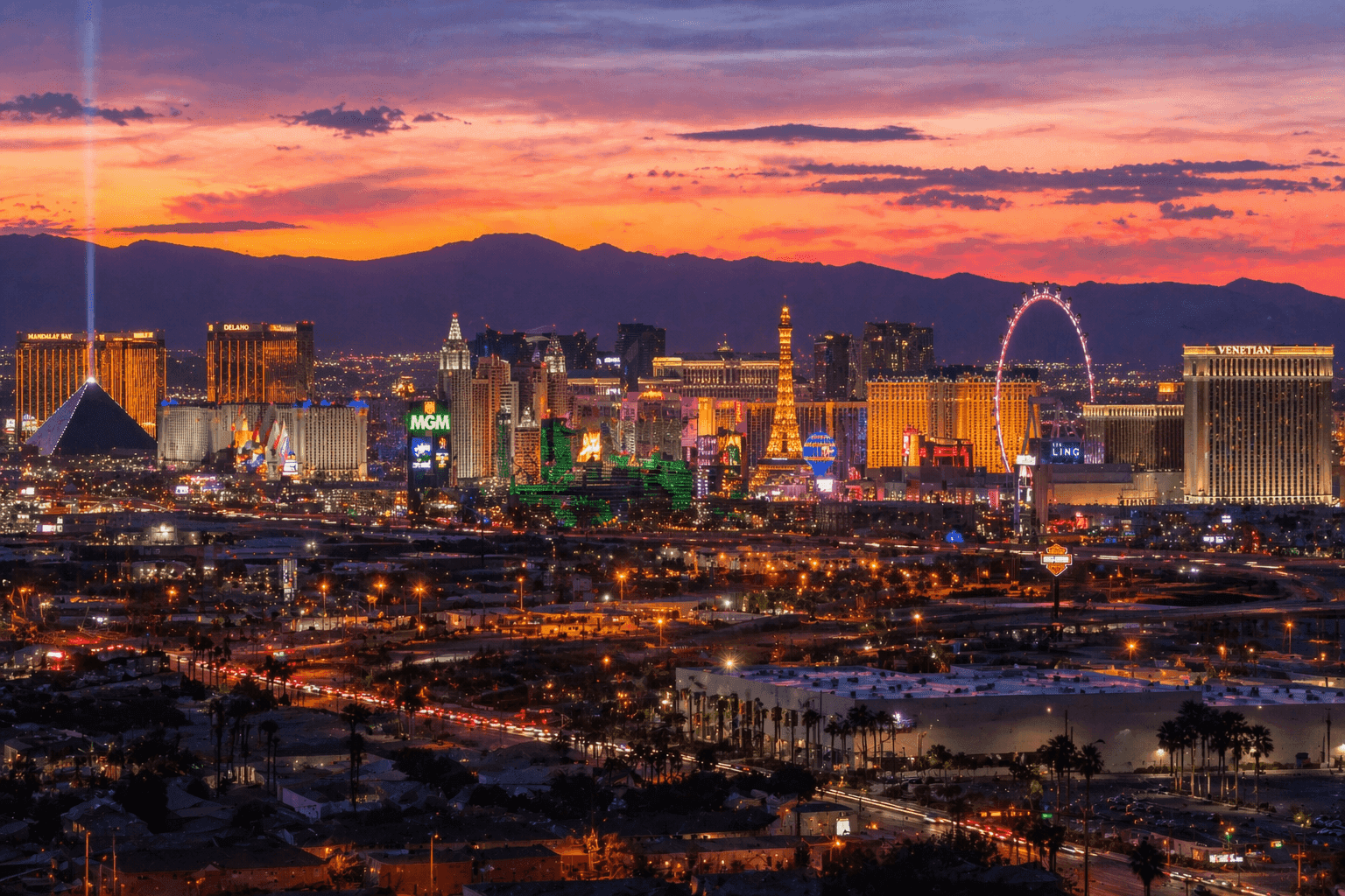 The Las Vegas skyline at dusk with the Strip's neon lights visible in the distance against a desert mountain backdrop.