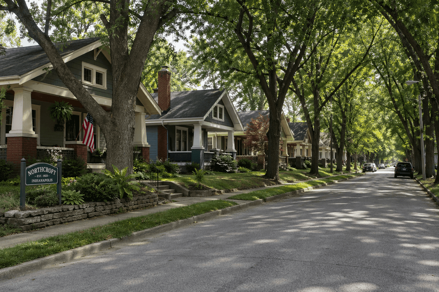 A quiet tree-lined residential street in the Northcroft neighborhood of Indianapolis, with craftsman bungalows and mature street trees.