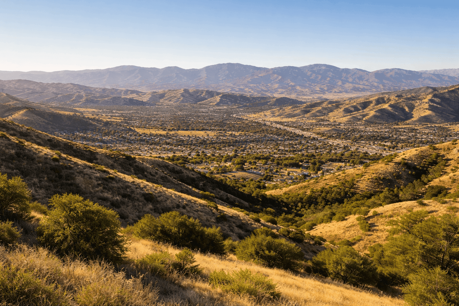 Rolling hills and mountains surrounding Santa Clarita, California, with the Santa Susana Mountains visible in the distance under a clear blue sky.
