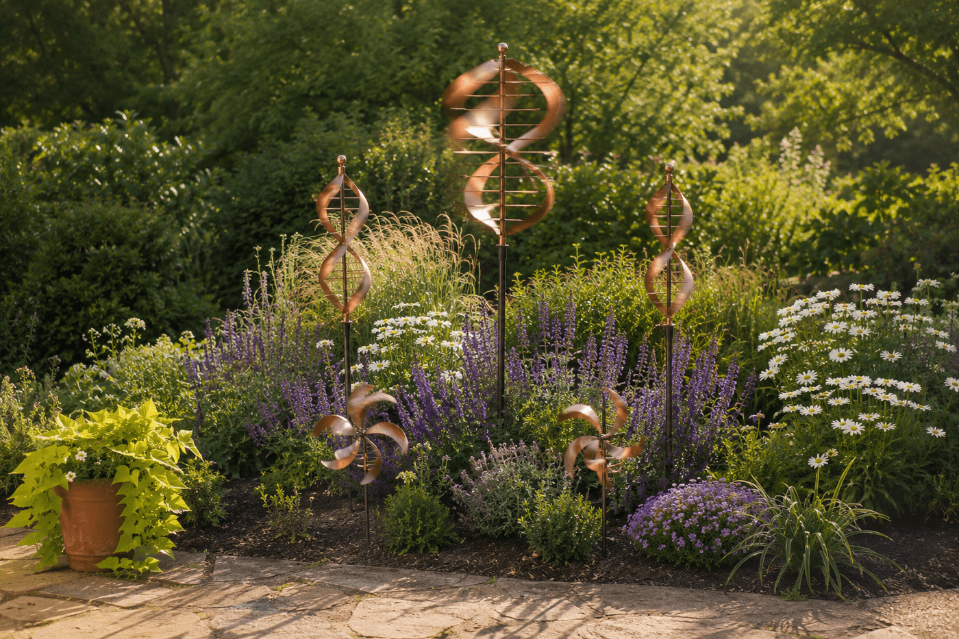 Wind garden installation in a lush garden bed featuring a tall copper spiral spinner on a five-foot stake at the back, two medium double-helix spinners at mid-height flanking it, and two small whirligigs at the front edge, all catching afternoon breeze against a backdrop of flowering perennials